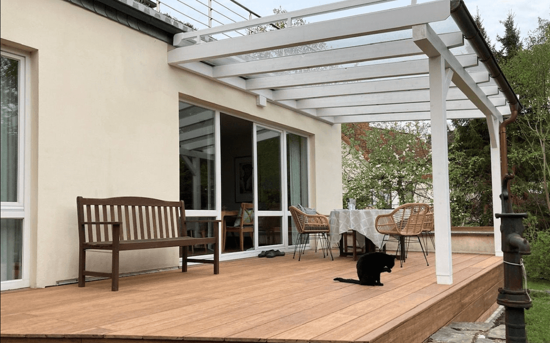Moderne Terrasse mit Closeddecking aMbooo Bambus Terrassendielen in warmem Holzton, überdacht von einer weißen Pergola, mit Sitzbank, Esstisch und Stühlen; ideale Kombination aus Langlebigkeit, Design und natürlicher Optik.