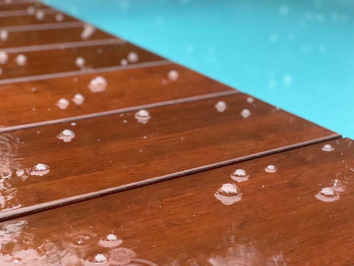 Wasserabweisende Holzterrasse am Pool mit dunklen Bambus Terrassendielen und sichtbaren Regentropfen. Die hochwertige Terrassenoberfläche zeigt ihre natürliche Holzoptik und Witterungsbeständigkeit.