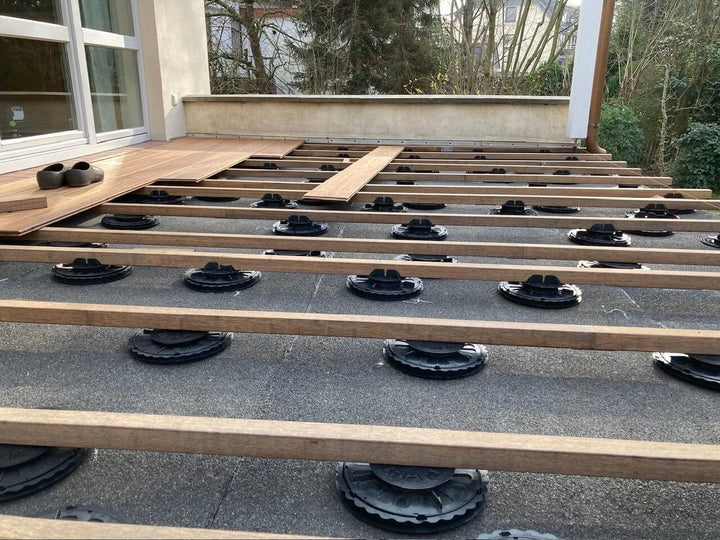 Terrassenunterkonstruktion aus Bambus auf höhenverstellbaren Stelzlagern während der Verlegung von Terrassendielen. 