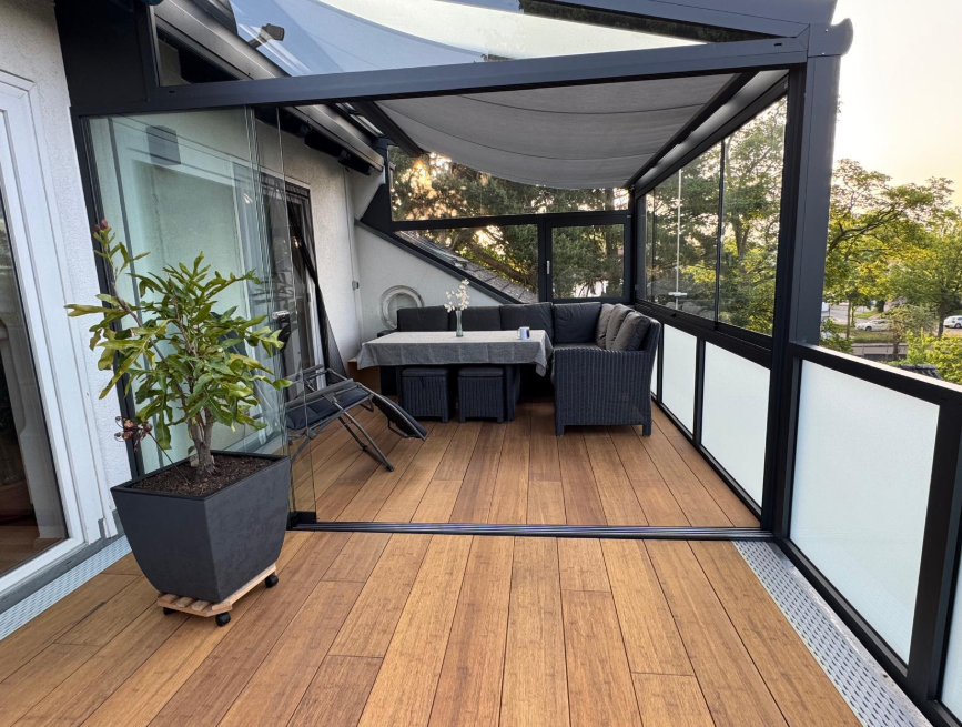 Die aMBOOO Bambusdiele Cristobal  unter moderner Überdachung an einem Einfamilienhaus, ausgestattet mit Gartenmöbeln. Nachhaltige Bambusdielen mit natürlicher Holzoptik, ideal für stilvolle und wetterfeste Terrassengestaltung.