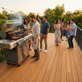 Freunde feiern bei Sonnenuntergang eine Grillparty auf einer großzügigen Bambusterrasse mit Lichterkette und Blick ins Grüne.