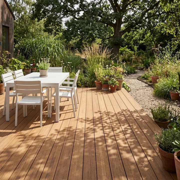 Sonnige AMBOOO-Terrasse mit weißer Sitzgruppe, Topfpflanzen und Blick in einen üppig bepflanzten Naturgarten.