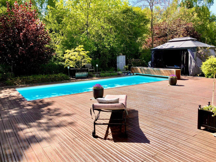 Großzügige Terrasse mit hochwertigen ambooo Bambus Terrassendielen, integriertem Pool, Sitzlounge und Sonnenschirm in einem gepflegten Garten.