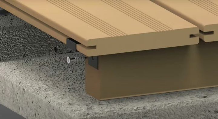 Detailansicht einer verdeckten Randbefestigung für Terrassendielen. Die erste Diele wird mit einem seitlich montierten Metallhalter auf der Unterkonstruktion befestigt und verschraubt, sodass keine sichtbaren Schrauben auf der Dielenoberseite vorhanden sind.