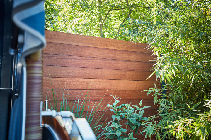 Privater Rückzugsort im Garten mit sonnenbeschienener Sichtschutzwand aus Bambus, viel Grünpflanzen und einem Strandkorb.