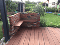 Moderne Terrasse mit rötlich-braunen Bambus-Terrassendielen und einer integrierten Sitzecke aus Klinkermauerwerk im gepflegten Garten.