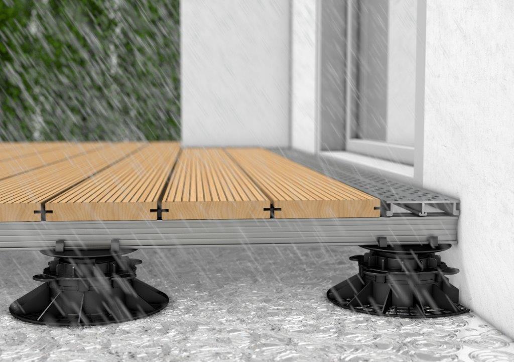 Technische Darstellung einer Terrassen-Drainage am Wandanschluss unter Holzdielen auf Stelzlagern.